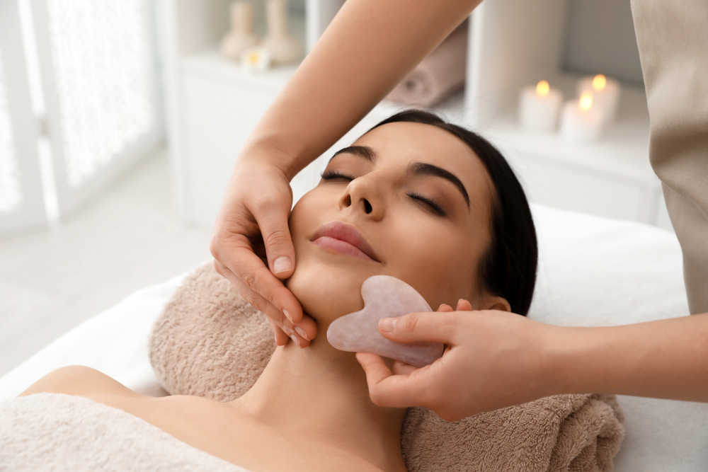 Young,Woman,Receiving,Facial,Massage,With,Gua,Sha,Tool,In